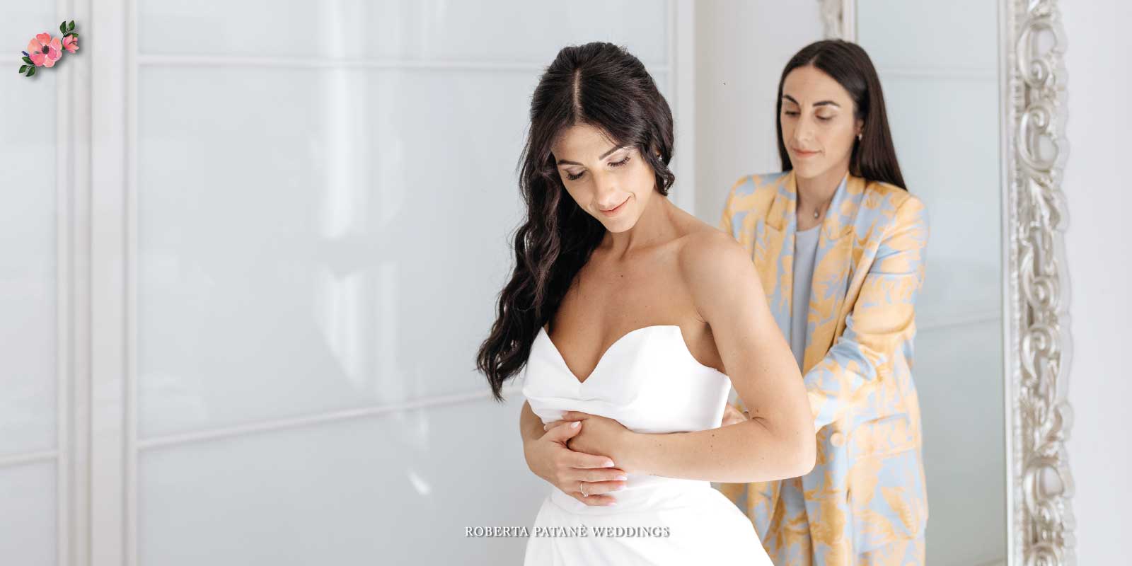 Preparazione-della-sposa_Roberta-Patane-Weddings Una sposa che si sta preparando con la testimone che l'aiuta ad allacciare l'abito